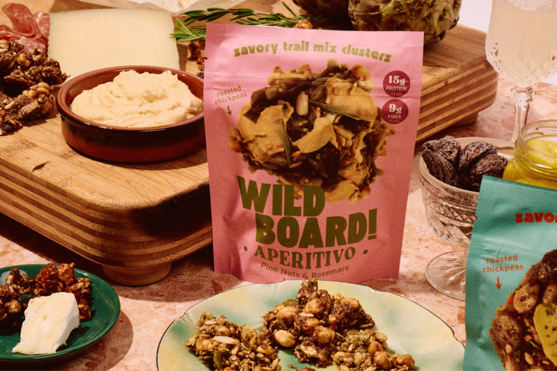 An appetizer board with cheese, dips and a WildBoard Aperitivo pouch of savory trail mix clusters